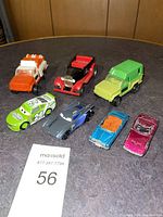 Seven toy vehicles arranged on dark surface: 3 Tonka trucks and 4 die-cast cars including race and sports cars.