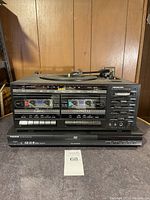 Front view of dual cassette tape deck showing AM radio tuner, tape compartments, and control buttons with Toshiba DVD player below.