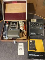 Lot overview showing Kodak Colorburst 350 instant camera with manual, Kodak Colorburst 320 instant camera, a vintage Kodak folding camera in case, GE M3 battery pack, and accessories.