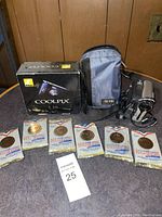 Full lot showing Nikon Coolpix L18 box, camera bag, video camera, and several packet items on a table