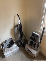 Overview photo showing the vintage upright Kirby vacuum alongside two boxes containing various attachments and accessories including a carpet sweeper unit.