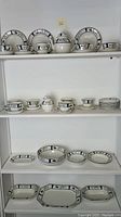 Full set arranged on shelves showing all pieces including plates, cups, sugar bowl, creamer, and serving platter