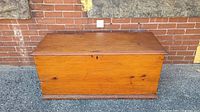 Front view of antique wooden blanket chest against a brick wall showing wood grain and keyhole on closed lid.