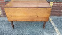 Closed view of antique wooden drop leaf dining table with visible wood grain and turned legs.