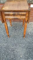 Front view of antique wooden drop leaf table showing the drawer and turned legs with some wear.
