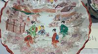 Scalloped bowl with painted Asian scene of figures and landscape, floral decoration around edges.
