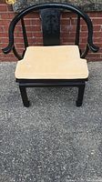 Full view of black wooden Chinese Ming style armrest chair with beige cushion seat placed outside on pavement.