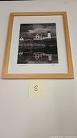 Framed photoscape art print showing lighthouse scene with reflections and buildings, includes frame and matte, with visible pencil signature and edition number 89/99.