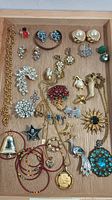 Overview of costume jewelry pieces including earrings, brooches, necklaces, and pendants arranged on wooden tray