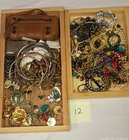 Two wooden trays containing a brown leather purse and various costume jewelry pieces including necklaces, bracelets, bangles, earrings, and chains.
