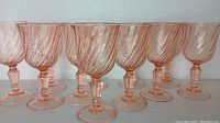 Row of nine pink swirl crystal cordial glasses, showing the bowl, stem and base design