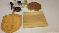 Photo showing wooden cutting boards, woven basket, glass measuring cup, metal garlic press, grater, and small kitchen accessories arranged on a white surface