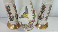 Close-up of the porcelain vase with bird and flower design flanked by two porcelain candle holders with brass bases and decorative reliefs.