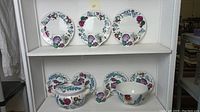 Three dinner plates with floral designs arranged on shelf with two smaller salad plates supporting them.