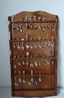 Full view of wooden rack with three rows holding 28 souvenir advertising spoons, various designs and colors visible.