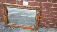 Front view of the rectangular vintage mirror leaning against a brick wall, showing detailed wood carvings on the oak frame surrounding the mirror glass