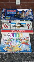 Three vintage board games stacked with visible titles: Mad Scientist Monster Lab by Mattel, The Game of Life, and Monopoly
