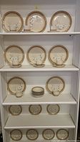Display of stoneware china set arranged on shelves including mugs, saucers, bowls, salad and dinner plates with floral pattern and brown rims.