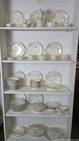 Full display of entire china collection arranged on four shelves showing plates, bowls, teapot, casseroles, creamer, sugar bowl, gravy boat and cups with saucers.