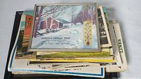 Stack of postcards topped with framed advertising thermometer showing a winter scene with snow and thermometer scale attached.