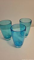 Three blue translucent plastic glasses, glossy finish, shown upright on a surface with neutral background.