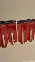 Set of four battery operated candle lamps, packaged, showing front view with all four lamps upright.