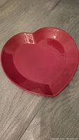 Top-down photo of a glossy red heart-shaped plate on a gray surface.
