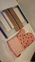 Photo showing white and blue cutting board with white kitchen towel attached and a pink floral oven mitt in original packaging.