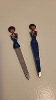 Photo of nail file and tweezers shaped as a brunette lady in a blue dress on a white background showing details of design and size.