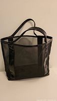Front and side view of black mesh and vinyl tote bag standing upright on a flat surface, displaying its size and shape clearly.