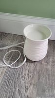 Cream color wax melt warmer resting on a gray wood floor showing textured exterior and electrical cord.