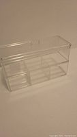 Photo of clear rectangular storage box showing its transparent hard plastic construction and divided compartments.