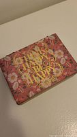 Closed view of floral box with gold lettering that says 'Choose Happy Be Happy'.