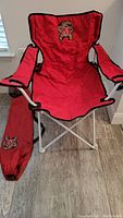 Red vinyl University of Maryland tailgate chair with white metal legs and matching carrying bag with printed logos.