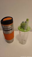 Front view of adult stainless steel mug with orange grip and kids water bottle with frog lid and straw