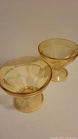Pair of yellow glossy plastic dessert glasses shown side by side with pedestal bases and flared tops.