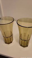 Pair of yellow glossy plastic drinking glasses on a white surface, showing full height and faceted design
