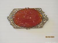 Front view of antique Chinese silver brooch with carved carnelian stone, showing detailed carving and silver frame.