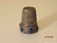 Front angle view of antique silver thimble showing lapis lazuli stones around the base, one stone missing.