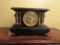 Front view of antique black mantel clock with gilt accents and columns, showing winding key in front.