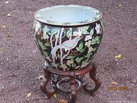 Full view of the porcelain planter bowl on the wooden stand showing the exterior floral and bird design on a black background.