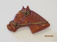 Front view of a carved Bakelite horse head brooch in butterscotch color with carved details and metal bridle hardware.
