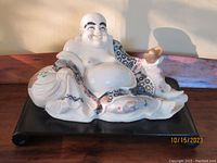 Front view of the seated Buddha sculpture on the black scroll platform base showing detailed painted robe and gold vessel in hand.