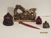 Front view of the gold-colored Chinese sea dragon surrounded by three Buddha figurines and a red letter opener placed in front of them.