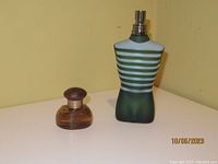Two men's cologne bottles side by side on a surface, one Tommy Bahama and one Jean Paul Gaultier torso-shaped bottle.
