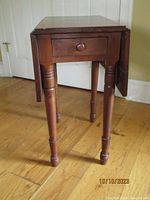 Front angled view of vintage drop leaf side table showing single drawer and turned legs