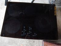 Top view of black glass ceramic surface induction cooktop showing four circular heating zones and touch control panel with icons and power indicators.