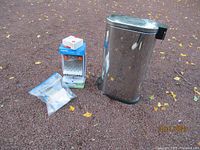 Photo showing a stainless steel step waste basket, a small box, and a plastic bag with small items, representing some of the smaller miscellaneous home goods in the lot.