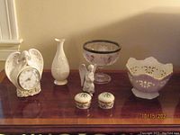 Photo showing altogether a white angel clock, Lenox bud vase, pierced white bowl, angel figurine, and two small trinket boxes on a wooden surface.