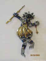 Front view of the Liztech dancer brooch showing the detailed figure holding a gold-tone staff, with blue wire accents and metallic gold skirt over painted body.